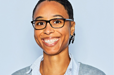 A portrait of Stefani Thomas, PhD, smiling. Stefani wears black glasses, a white collared shirt with a grey cardigan over the top. Her hair is pulled back. 