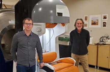 Professor Michael Garwood (right) and colleague Ben Parkinson (left) pose standing on either side of the portable MRI machine.