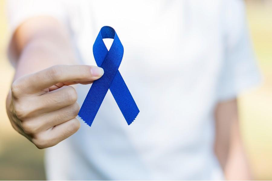 A man in a white t-shirt holds a royal blue ribbon signifying colorectal cancer awareness.