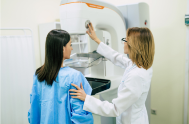 Female doctor showing a mammography machine to a female patient in gown